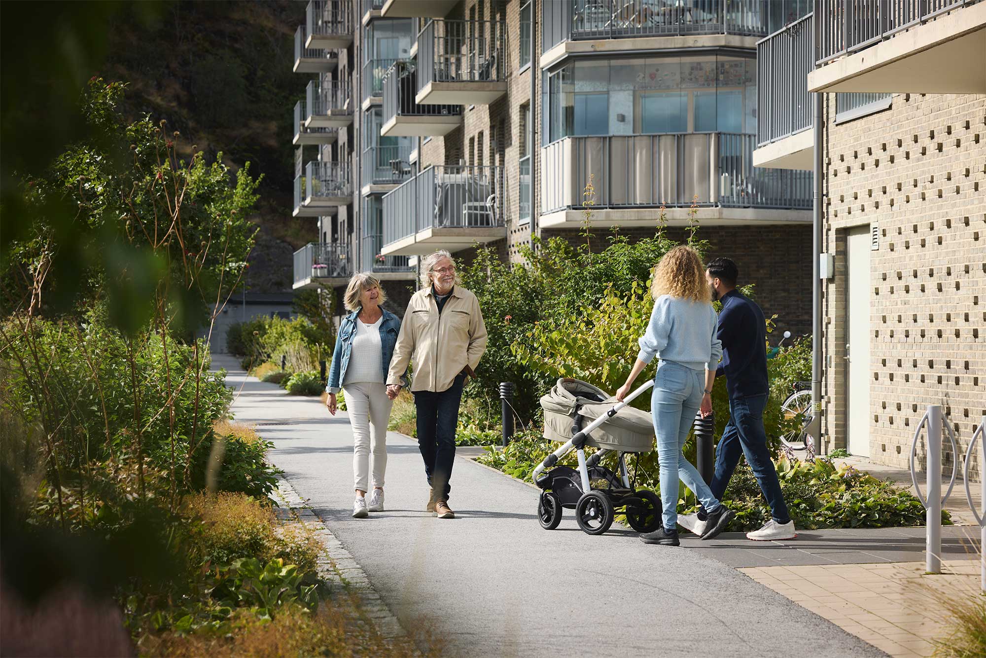 Äldre och ungt par med barnvagn går i bostadsområde